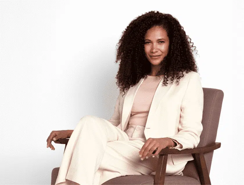Woman with curly dark hair sitting with her legs crossed looking confidently at the camera
