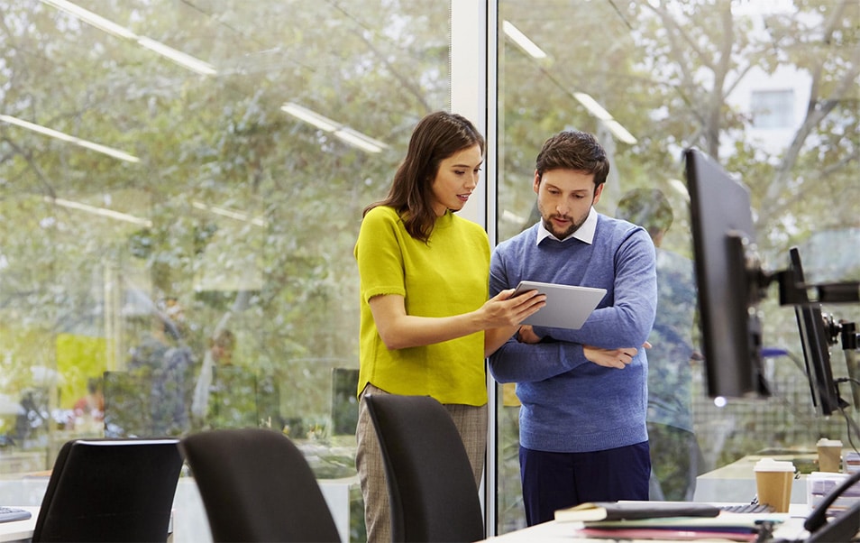 Professional looking woman in a yellow sweater showing her colleague something on her tablet