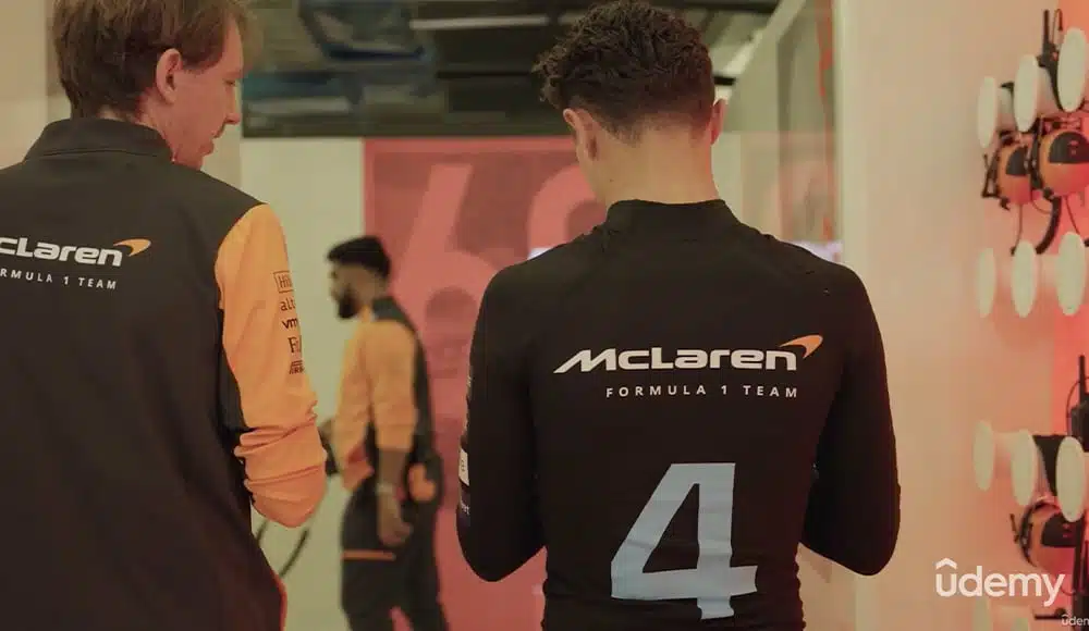 Candid photo of a McLaren engineer standing and talking with a McLaren race car driver